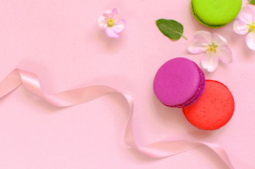 Cake macaron or macaroon with pink gift ribbon spring flowers on pink background top view flat lay, beautiful dessert, colorful almond cookies, pastel colors