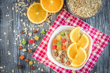 Homemade oatmeal porridge with orange, candied fruit and hazelnut on grey wooden background. Healthy breakfast.