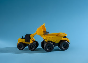Fototapeta na wymiar Yellow toy bulldozer loading money to the yellow toy truck. Space for text placement. 