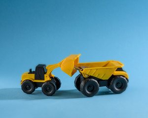 Yellow toy bulldozer loading money to the yellow toy truck. Space for text placement. 