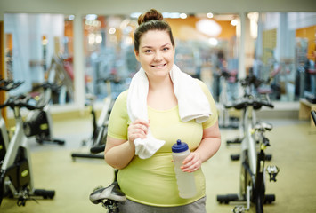 Happy plump female with bottle of water and towel looking at you with smile