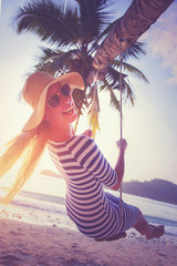 Young woman swinging on the beach and smiling into camera at sunset. Vacation concept. Retro styled colors.