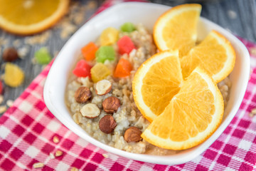 Homemade oatmeal porridge with orange, candied fruit and hazelnut on grey wooden background. Healthy breakfast.