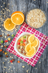 Homemade oatmeal porridge with orange, candied fruit and hazelnut on grey wooden background. Healthy breakfast.