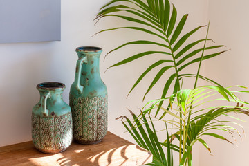 Two decorative vases on wooden table and Majesty Palm in sunlight - cozy home scene