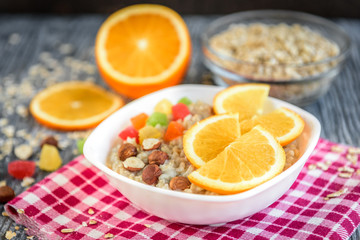Homemade oatmeal porridge with orange, candied fruit and hazelnut on grey wooden background. Healthy breakfast.