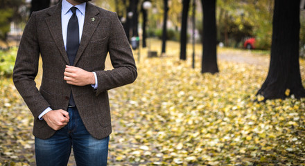 Man in custom tailored suit posing outdoors in autumn and buttoning his coat