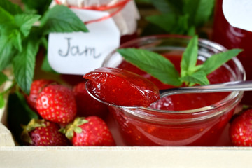 Strawberry jam in glass jars surrounded by the berries and mint in a wooden box