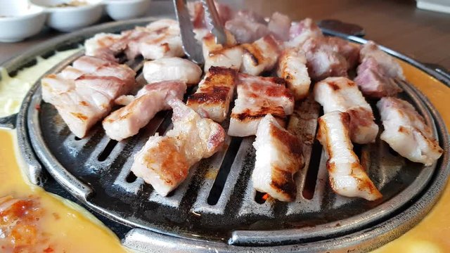Pork sliced grill and barbecue on a pan and tood tongs for cooking. The side of pan have a omelette and Cheese.Korean Barbecue (BBQ)