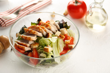 salad cesar with chicken grill in glass bowl on white wooden table. Decor fresh vegetables