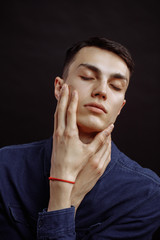 Portrait of young attractive guy posing with closed eyes. He is touching his face while checking quality of his skin. Masculine beauty concept. Copy space