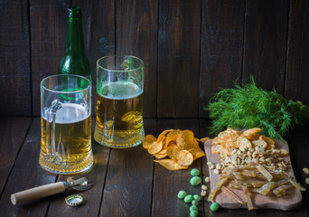 Snacks to beer, on a wooden board and two mugs of beer. Chips, peanuts, pieces of fish,crackers,...