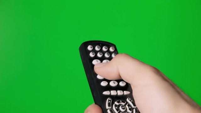 A male hand operating a tv remote control on a green background.
