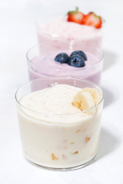 sweet yoghurts with fruits and berries on white table, vertical