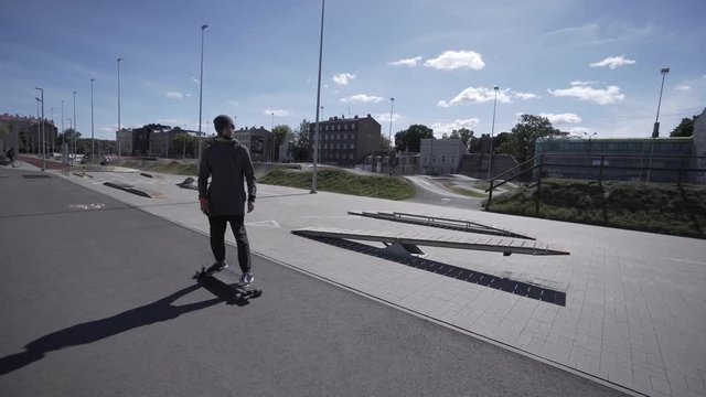 Electric Longboard man in sweatshirt and hat ride on red sport stadium with playground