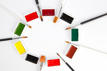 Solid watercolors pans with various paint brushes arranged in circle with copy space on white background