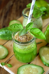 Green cocktail in a glass jar sprinkled with brans decorated with basil against the wooden background