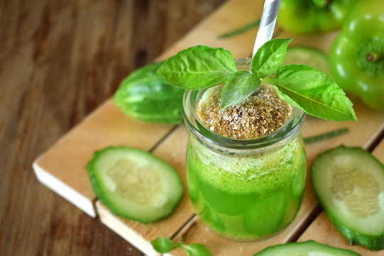 Green cocktail in a glass jar sprinkled with brans decorated with basil against the wooden background