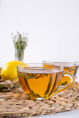 Thyme tea in glass cup, sprig of fresh thyme, lemon and ginger on white table background