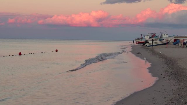 Bellissimo tramonto su spiaggia. Gabbiani volano e camminano sulla spiaggia.  Barche sulla destra. Cielo rosa tramonto