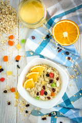 Homemade oatmeal porridge with honey, orange, raisin, peanut and candied fruit on white wooden background. Healthy breakfast.