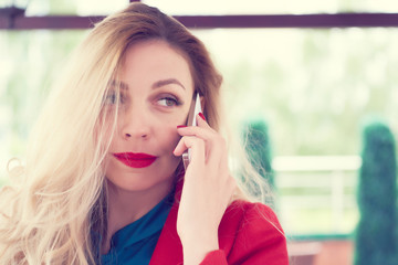 Smiling blonde female speaks on phone with a friend indoors summer cafe