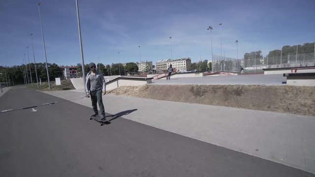 Electric Longboard man in green shirt and hat ride on red sport stadium with playground