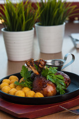 Fried potato balls with fried chicken legs with greens on a black plate on a wooden board. Restaurant menu.