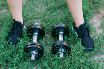 Dumbbells on green grass background and foots in black sneakers