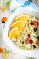 Homemade oatmeal porridge with honey, orange, raisin, peanut and candied fruit on white wooden background. Healthy breakfast.