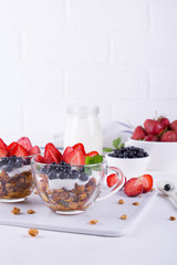 Healthy breakfast in a cup with homemade baked granola, fresh berries, and yogurt on a white table background