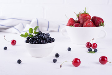 Fresh blueberriesand strawberry with green leaf  in a white bowl on a white background