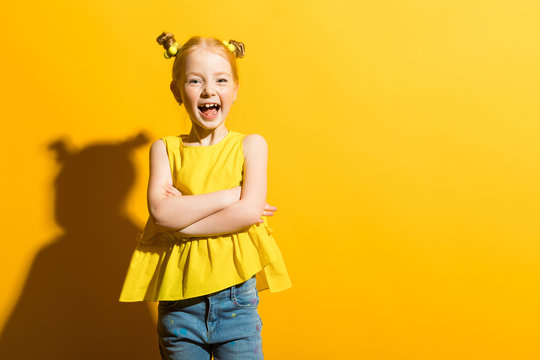 Girl with red hair on a yellow background. The beautiful girl laughs and folds her arms across her chest.