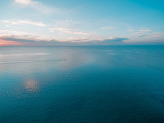 Tiny fishing boat sailing across calm sea at dusk