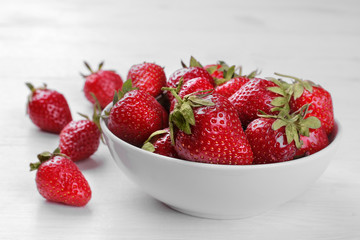 A lot of red strawberries in a white bowl on a white wooden background