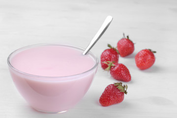 Strawberry yogurt in a glass bowl with strawberries on a white wooden background