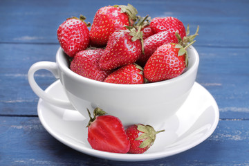 A lot of ripe, fresh strawberries in a white cup on a blue wooden background