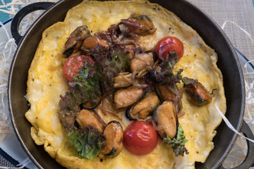 Omelet with mussels, cherry tomatoes and green onions on a ceramic plate on a black background.