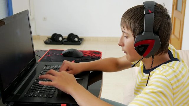 Teenager using laptop. Teen boy with headphones playing computer game at home with dumbbells in the background. Game addiction and hypodynamia concept