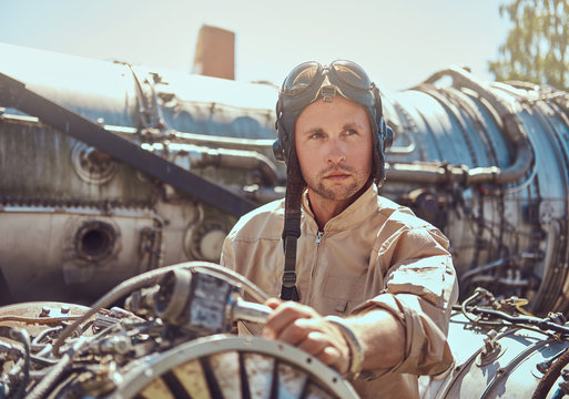 Portrait of a mechanic in uniform and flying helmet, repairing the dismantled airplane turbine in an open-air museum.