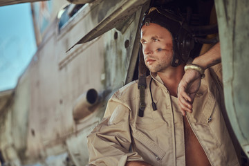 Portrait of a mechanic in uniform and flying near, standing under an old bomber airplane in the open air museum.