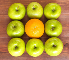 An orange between apples, standing out of the crowd concept.