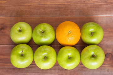 An orange between apples, standing out of the crowd concept.