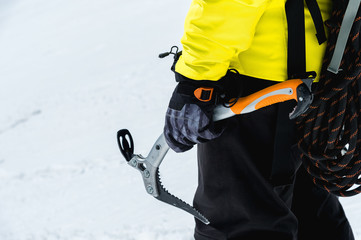 A mountaineer man holds an ice ax high in the mountains covered with snow. Close-up from behind....