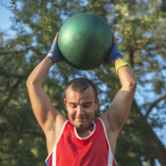 Young athlete performs sports exercises with a ball outdoors.