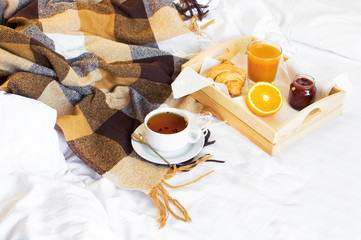 Breakfast Bed Cup of tea Croissant Orange juice Fresh orange Jam Wooden tray Bed linen Plaid in a cage Morning breakfast at the hotel Interior concept Top view Copy Space