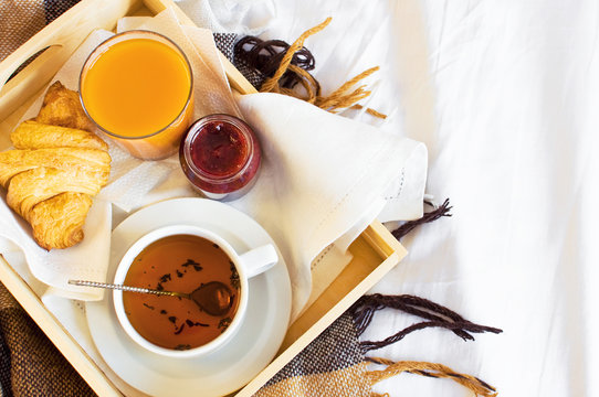 Breakfast Bed Cup of tea Croissant Orange juice Fresh orange Jam Wooden tray Bed linen Plaid in a cage Morning breakfast at the hotel Interior concept Top view Copy Space
