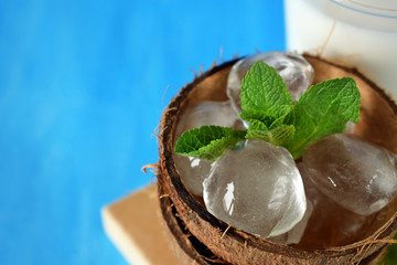 Coconut halves with ice cubes. A glass of coconut milk next to it. Ingredients for a tropical cocktail on blue background