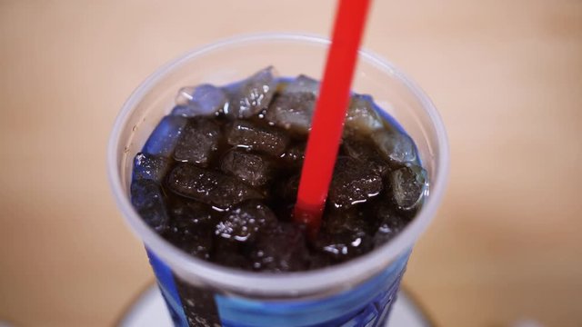 A top down shot of a red plastic straw in a cup of cola. Plastic straws have come under scrutiny lately for being bad for the environment. Shot at 60fps for optional slow motion use.  	