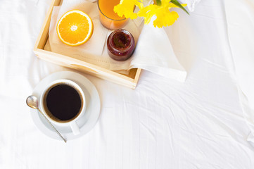 Morning breakfast in bed wooden tray with a cup of coffee croissant orange juice fresh orange jam...